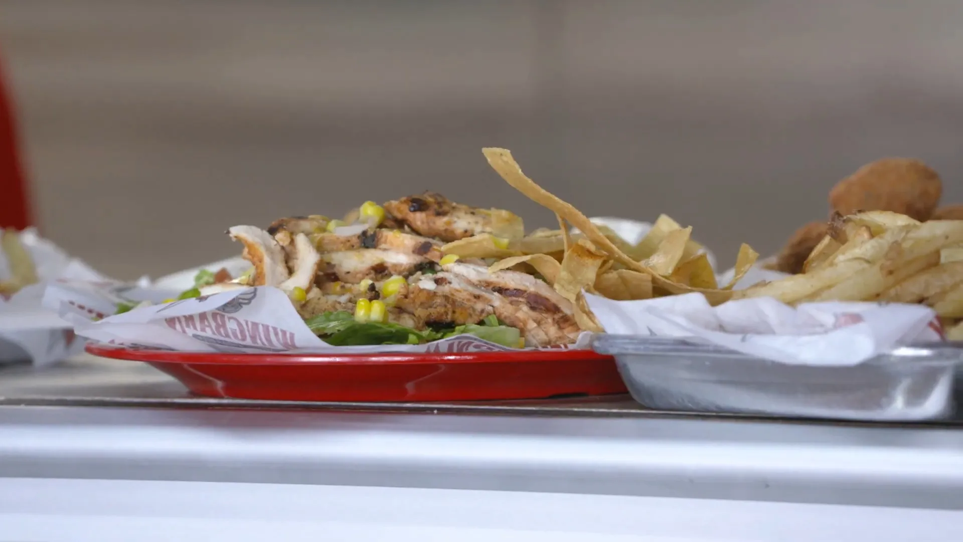 Close-up of plated restaurant food with grilled chicken, chips, and sides on a counter.